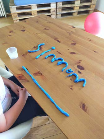 Un prénom modelé en pâte à modeler bleue sur une table en bois.